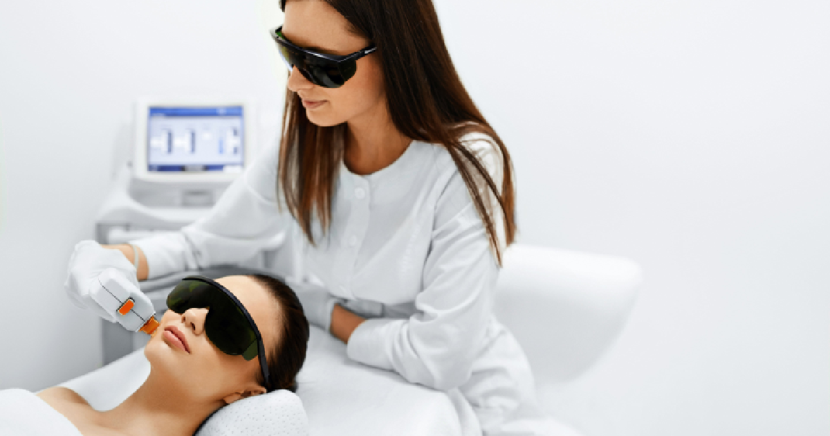 A skincare specialist performing a photofacial treatment on a female client using IPL (Intense Pulsed Light) technology. Both are wearing protective eyewear in a clinical setting in BOZEMAN, MT