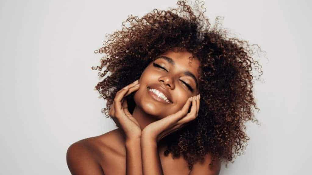 Pretty young girl with curly hair put her hands on her cheeks | Instinct Holistic Medical Spa in Bozeman, MT