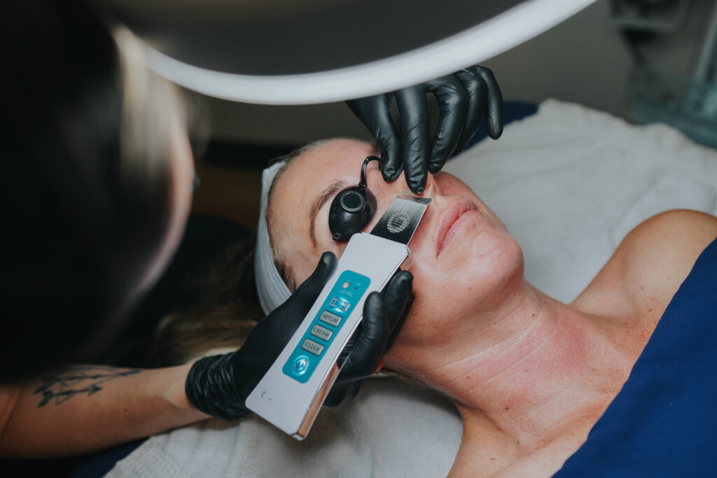 A practitioner providing facial extractions using an ultrasonic skin scrubber.